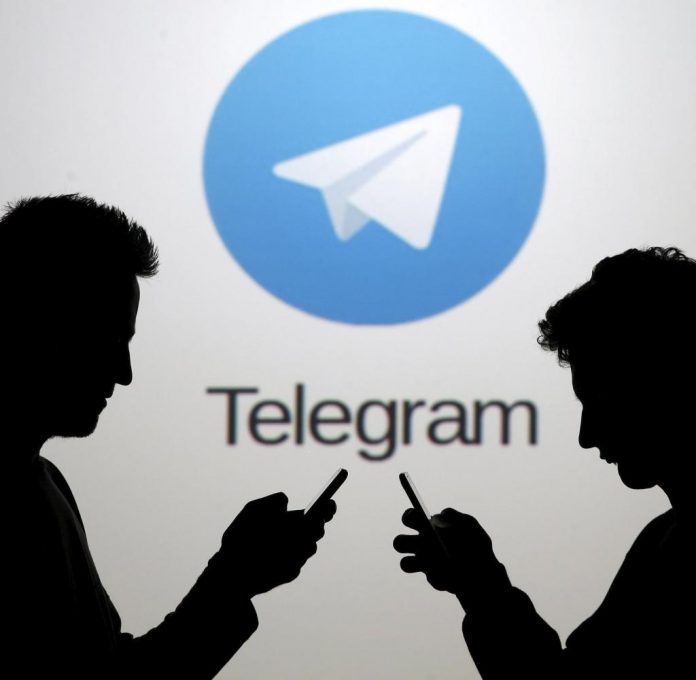 Two-men-pose-with-smartphones-in-front-of-a-screen-showing-the-Telegram-logo-in فرصتها و تهدیدهای تلگرام